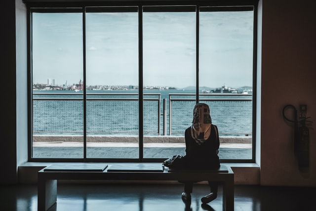 muslim woman siiting on a bench looking at the ocean on a big window
