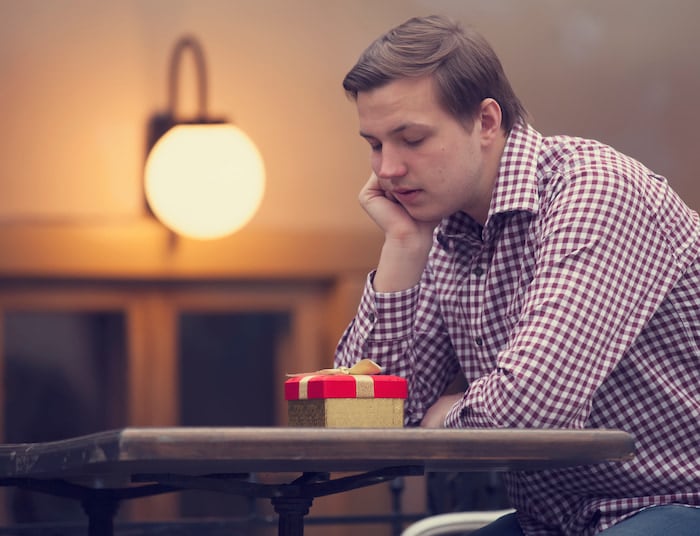 Sad man sitting in a café with a gift, feeling lonely